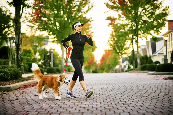 Young woman walking her don in a neighborhood with houses and trees in the background.
